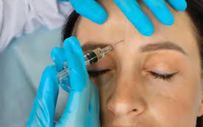 Close-up of a clinician in blue gloves injecting a syringe into a woman's forehead for cosmetic treatment.