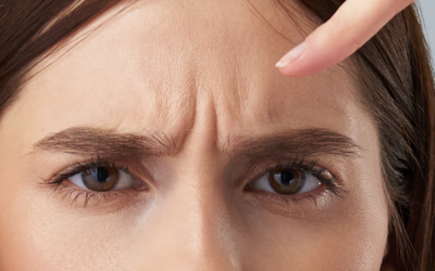 Close-up of a woman's face with a furrowed brow as she presses her forehead with a finger.