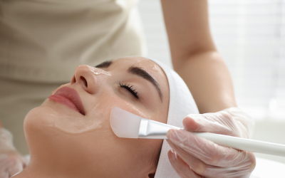 Woman relaxing with eyes closed as a skincare professional applies a facial mask with a brush on her face.